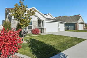 View of front of home with a front yard, an attached garage, driveway, and stone siding