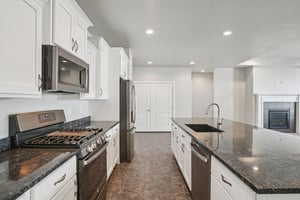 Kitchen featuring stainless steel appliances, white cabinetry, dark stone countertops, and recessed lighting