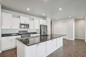 Kitchen featuring white cabinetry, an island with sink, recessed lighting, stainless steel appliances, and dark stone counters