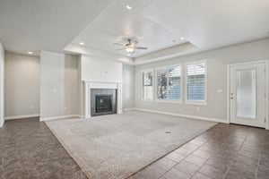 Unfurnished living room with a tray ceiling, dark carpet, a fireplace, and ceiling fan