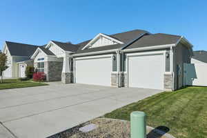View of front of property with stone siding, a front yard, a garage, and driveway