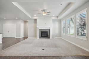 Unfurnished living room featuring a raised ceiling, a fireplace, a ceiling fan, and recessed lighting