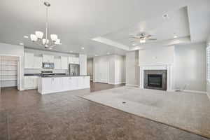 Unfurnished living room with a tray ceiling, a fireplace, ceiling fan, and a chandelier