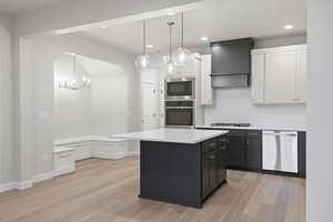Kitchen with dark cabinets, decorative backsplash, white cabinetry, hanging light fixtures, and appliances with stainless steel finishes