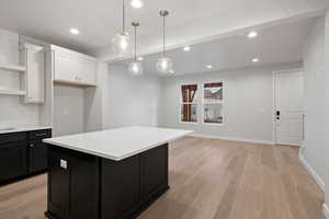 Kitchen featuring dark cabinetry, light wood-type flooring, recessed lighting, backsplash, and hanging light fixtures