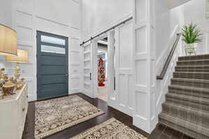 Entrance foyer with a decorative wall, stairway, dark wood-style flooring, a barn door, and a high ceiling