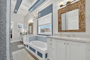 Primary Bathroom with two vanities, a bath, a chandelier, and dark tile patterned floors