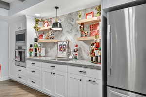 Kitchen with stainless steel appliances, white cabinetry, light wood-style flooring, pendant lighting, and a textured ceiling