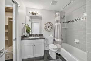 Full bath featuring vanity, dark tile patterned floors, a textured ceiling, shower / bath combination with curtain, and a spacious closet