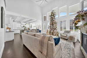 Living area with dark wood finished floors, beamed ceiling, a glass covered fireplace, a high ceiling, and ceiling fan