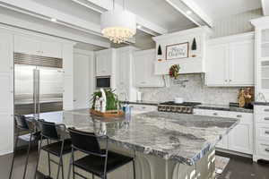 Kitchen featuring a breakfast bar, a center island with sink, pendant lighting, white cabinetry, and beam ceiling