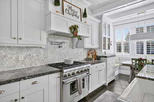 Kitchen featuring premium range, decorative backsplash, white cabinetry, dark wood-style flooring, and dark stone counters