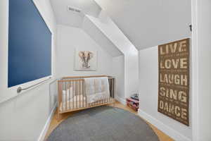 Bedroom with vaulted ceiling, a textured ceiling, a crib, and light wood-style floors