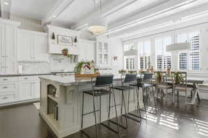 Kitchen featuring a kitchen breakfast bar, open shelves, dark stone counters, beamed ceiling, and white cabinetry