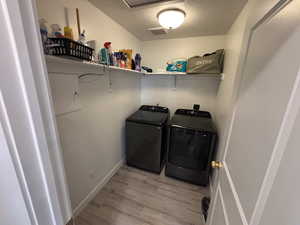 Washroom featuring a textured ceiling, light wood-type flooring, and washing machine and clothes dryer
