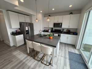 Kitchen with light wood finished floors, a breakfast bar, a kitchen island with sink, stainless steel appliances, and decorative light fixtures