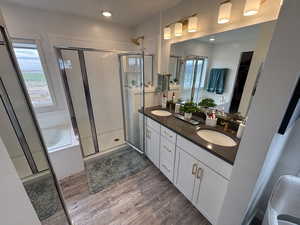 Full bath featuring double vanity, dark wood-style floors, a shower stall, and a bath