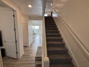 Staircase with a textured ceiling, wood finished floors, and recessed lighting
