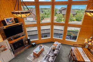 Carpeted living area featuring wood walls, a stone fireplace, and a high ceiling