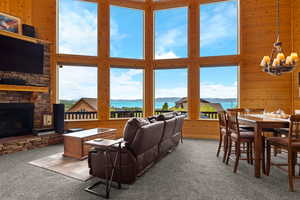 Living area with wood walls, a water and mountain view, a towering ceiling, carpet flooring, and a stone fireplace