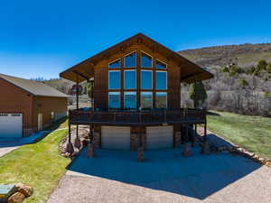 View of front facade featuring a wooden deck, stone siding, a front yard, driveway, and a garage