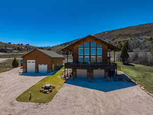 View of front of home with stone siding, a garage, a deck with mountain view, gravel driveway, and a front lawn