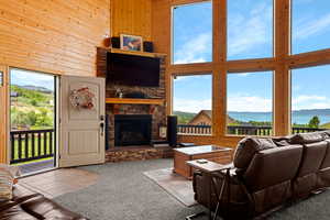 Living area featuring a high ceiling, a stone fireplace, light colored carpet, wooden walls, and light tile patterned floors