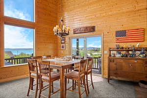 Dining area with wood walls, a towering ceiling, a water and mountain view, a chandelier, and carpet floors