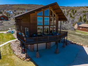 Rear view of house with a deck with mountain view, a lawn, stone siding, and a patio