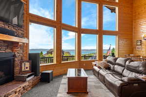Living area featuring wooden walls, carpet flooring, a fireplace, a high ceiling, and a water and mountain view