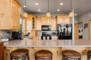Kitchen with a kitchen bar, light brown cabinetry, glass insert cabinets, decorative backsplash, and recessed lighting