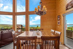 Dining room with a water view, wood walls, a towering ceiling, a chandelier, and tile patterned floors