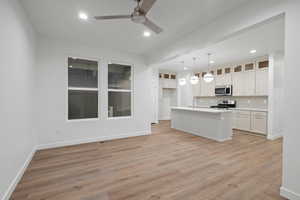 Kitchen featuring recessed lighting, light countertops, light wood-type flooring, a center island with sink, and decorative light fixtures