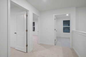Hallway with light colored carpet and baseboards