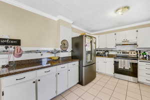 Kitchen with tasteful backsplash, stainless steel appliances, white cabinets, crown molding, and dark stone countertops