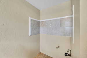 Bathroom with a textured wall, a textured ceiling, and tile patterned flooring