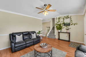 Living room with ornamental molding, stairs, light wood finished floors, vaulted ceiling, and a ceiling fan