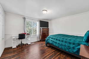 Bedroom with dark wood-style floors, ornamental molding, and an office area