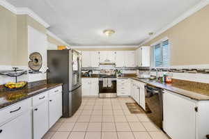 Kitchen featuring appliances with stainless steel finishes, white cabinets, a textured ceiling, backsplash, and dark stone countertops