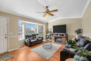 Living area with ornamental molding, wood finished floors, lofted ceiling, a ceiling fan, and a glass covered fireplace