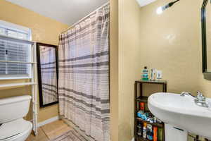 Full bathroom featuring a textured wall, curtained shower, and light tile patterned flooring