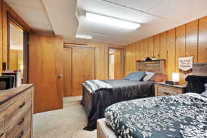 Bedroom with a closet, light colored carpet, wooden walls, and a drop ceiling