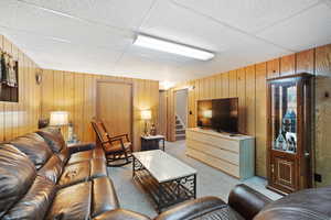 Living room featuring stairway, wood walls, light carpet, and a paneled ceiling