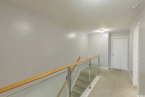 Hallway featuring an upstairs landing, light colored carpet, and a textured ceiling