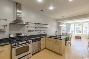 Kitchen with appliances with stainless steel finishes, wall chimney range hood, a peninsula, dark stone countertops, and hanging light fixtures