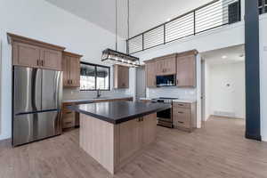 Kitchen with stainless steel appliances, decorative backsplash, dark countertops, a kitchen island, and a high ceiling