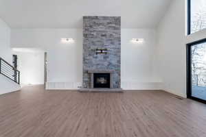 Unfurnished living room featuring a stone fireplace, light wood-style flooring, high vaulted ceiling, stairs, and a decorative wall