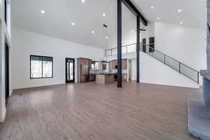 Unfurnished living room featuring beam ceiling, high vaulted ceiling, light wood-style floors, and recessed lighting