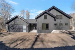 View of front of house featuring an attached garage, dirt driveway, and board and batten siding