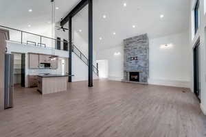 Unfurnished living room with high vaulted ceiling, light wood-style floors, a stone fireplace, a ceiling fan, and stairs